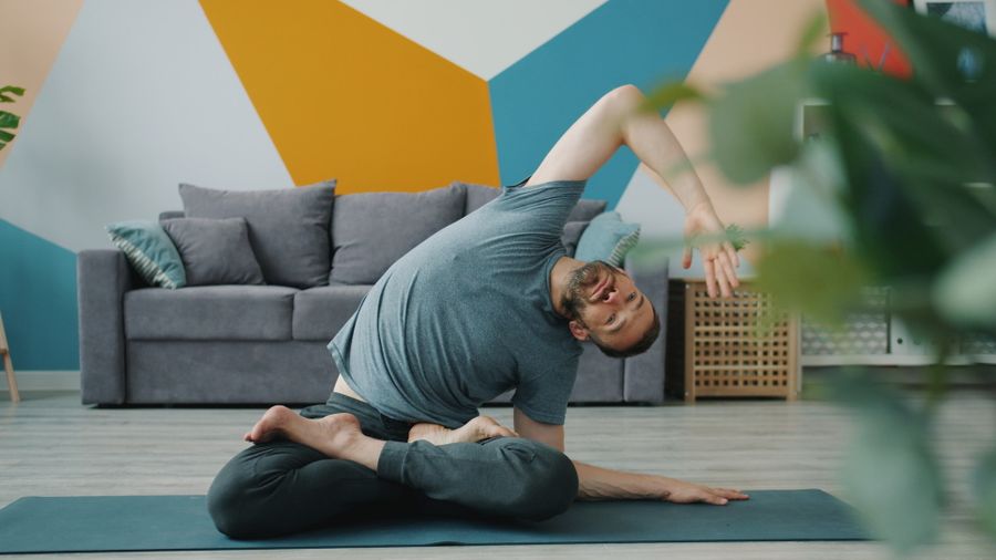 Man sitting on a living-room mat stretching his hip