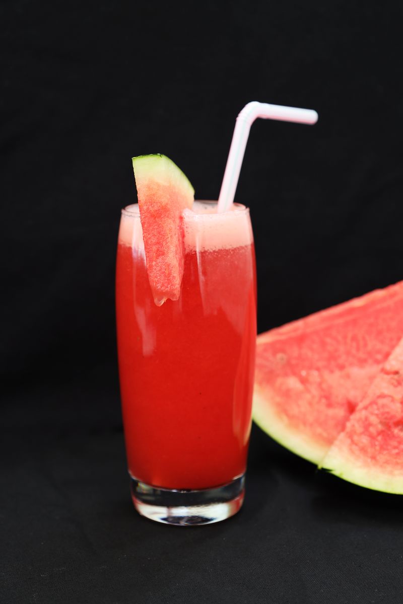 Glass of watermelon juice with a straw next to a slice of watermelon