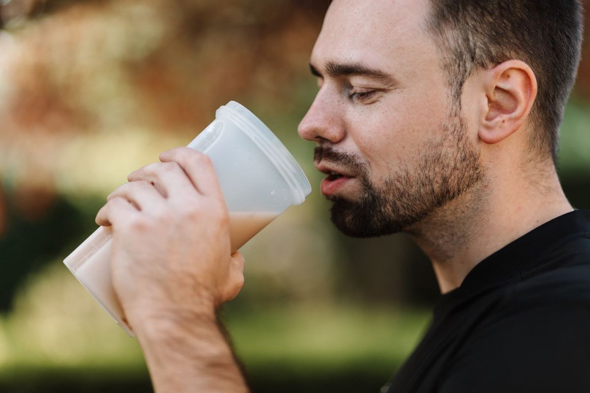 Bearded man drinking a smoothie from a glass outdoors