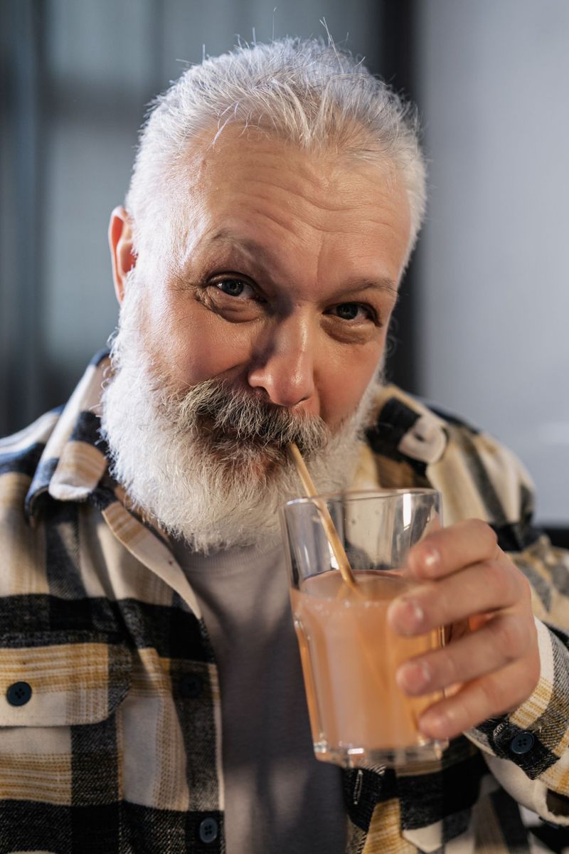 Older man with a grey beard drinking a smoothie through a straw