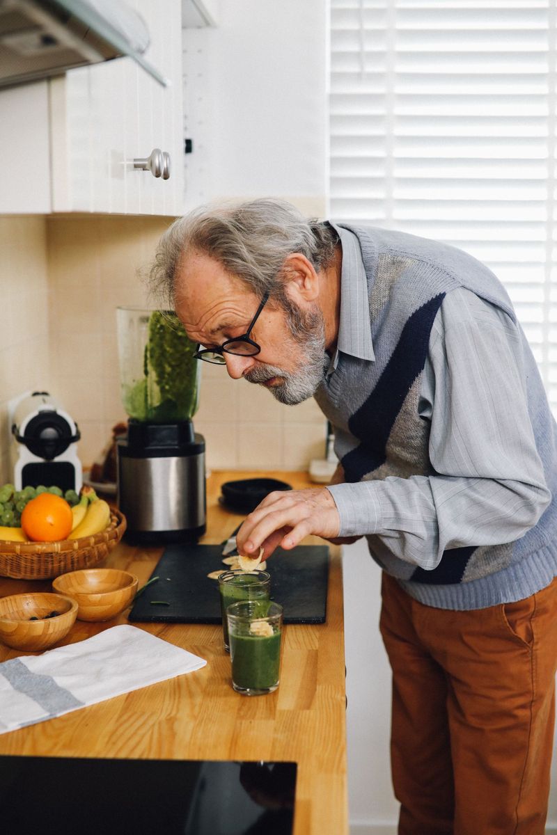 Older man preparing a green smoothie in his kitchen
